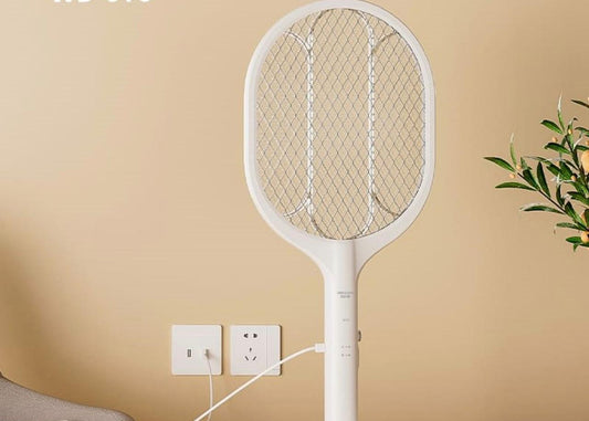 White electric fly swatter on a table against a beige wall.